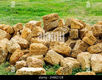 Une pile de pierre de construction de roche sur une pelouse verte est dispersée dans le désordre.Pierre de construction jaune, extraite dans les catacombes. Banque D'Images