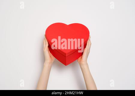 Mains tenant une grosse boîte rouge en forme de coeur.Bannière tendance pour la Saint-Valentin, la Journée internationale des femmes ou la Fête des mères.Gros plan sur la bannière Banque D'Images
