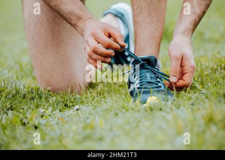Un gros plan d'un homme qui fixe les lacets de ces chaussures de sport sur l'herbe verte avant de s'entraîner Banque D'Images