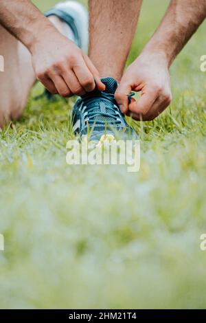 Un gros plan d'un homme qui fixe les lacets de ces chaussures de sport sur l'herbe verte avant de s'entraîner Banque D'Images
