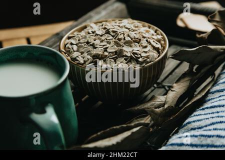 Un gros plan d'un bol rempli de graines d'avoine sur une table en bois sur des tons moody Banque D'Images