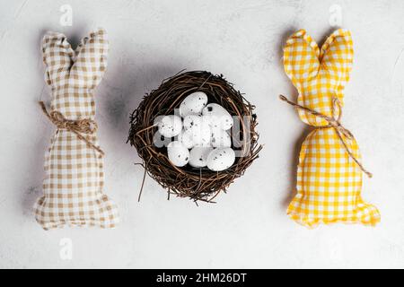 Composition de Pâques composée de deux lapins carrés faits main de couleur marron, blanche et jaune avec foulard sur fond de papier blanc et oeuf de caille à pois blancs Banque D'Images
