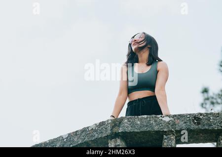 Jeune fille arabe dans un balcon sur des vêtements de sport pendant une journée ensoleillée, souriant et regardant loin de l'appareil photo avec l'espace de copie, image à l'envers Banque D'Images