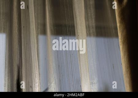 Le vent de flou artistique souffle à travers la fenêtre de la pièce.Agitant de la tulle blanche près de la fenêtre.Le soleil du matin éclaire la pièce.Sombre.Hors foyer. Banque D'Images