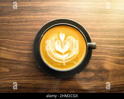 Magnifique café chaud latte art design mousse à l'intérieur de la tasse noire avec fond en bois.Vue de dessus Banque D'Images