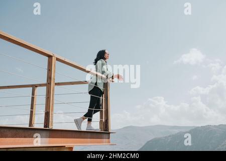 Femme dans un balcon sur une rivière massive et les montagnes vivant le moment liberté et liberté concept, bien-être pendant une journée ensoleillée Banque D'Images