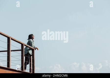 Femme dans un balcon sur une rivière massive et les montagnes vivant le moment liberté et liberté concept, bien-être pendant une journée ensoleillée Banque D'Images