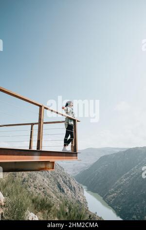 Femme dans un balcon sur une rivière massive et les montagnes vivant le moment liberté et liberté concept, bien-être pendant une journée ensoleillée Banque D'Images