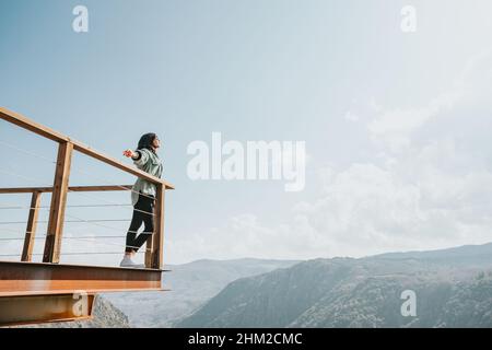 Femme dans un balcon sur une rivière massive et les montagnes vivant le moment liberté et liberté concept, bien-être pendant une journée ensoleillée Banque D'Images