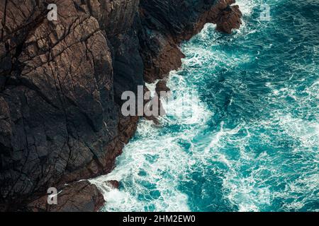 Un fond coloré de l'eau se brisant contre les pierres sur la côte de l'espagne Banque D'Images