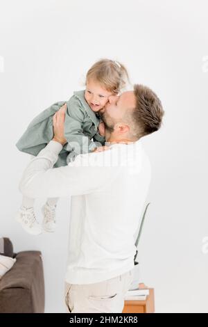 Portrait d'un jeune père élégant qui embrasse la petite fille à la joue, la tenant dans les bras.Beau père embrassant doucement sa belle fille de bébé, appréciant Banque D'Images