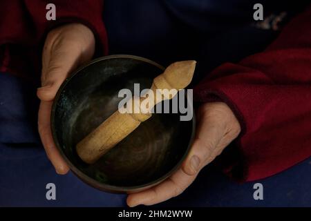Mains jouant chantant bol. Une femme anonyme tient un bol de chant dans ses mains tout en étant assise. Banque D'Images