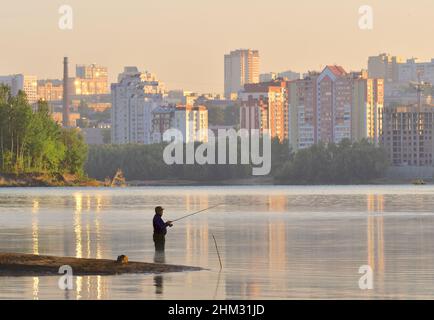 Novosibirsk, Sibérie, Russie - 10.05.2019: Pêcheur avec une canne à pêche genou-profondément dans l'eau à l'aube. Matin sur la rivière OB, à la maison sur la banque o Banque D'Images