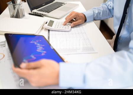 Homme au travail Conepte l'homme de bureau tenant la tablette et appuyant sur la calculatrice tout en étant assis dans le bureau. Banque D'Images