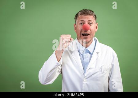 Le scientifique à la couche blanche a le nez de clown rouge et se tient devant le fond vert Banque D'Images