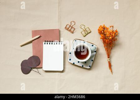 Bloc-notes, crayon, tasse de café, clip, fleurs sèches sur fond de tissu beige. Vue du dessus, espace copie Banque D'Images