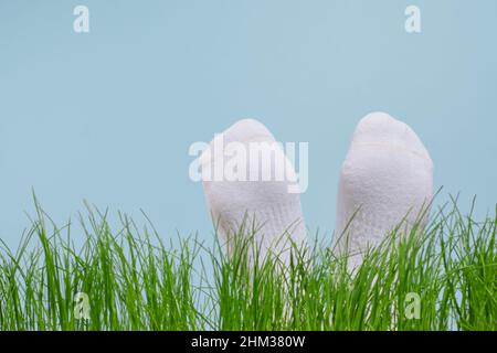 Les pieds des enfants portent des chaussettes blanches sur l'herbe verte sur un fond bleu, isolé. Concept de taches sales sur les vêtements blancs.Photo de haute qualité Banque D'Images