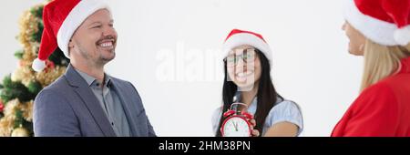 Groupe de gens d'affaires donnant des cadeaux de nouvel an et tenant le réveil rouge près de l'arbre de Noël Banque D'Images