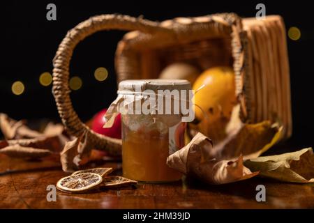 Un pot de confiture de pêche avec des tranches d'orange séchées avec un panier en osier renversé et des feuilles sèches en arrière-plan Banque D'Images