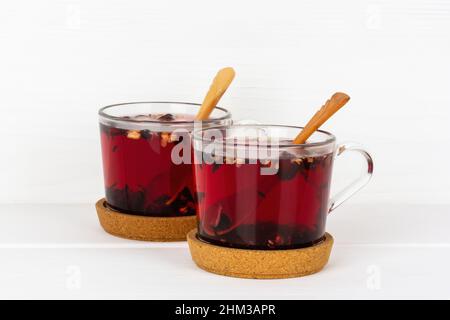 deux tasses de thé aux baies et aux fleurs avec des cuillères en bois sur des supports en liège sur une table blanche en gros plan Banque D'Images