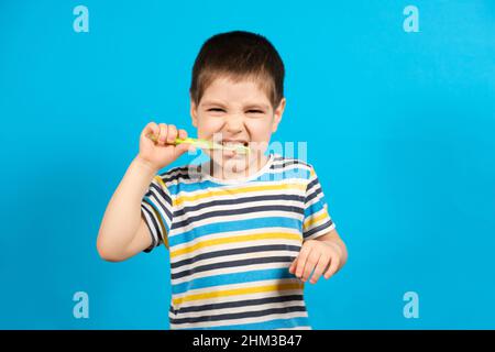 Magnifique enfant heureux en T-shirt rayé brosses dents avec une brosse à dents verte sur fond bleu, espace de copie pour le texte. Banque D'Images