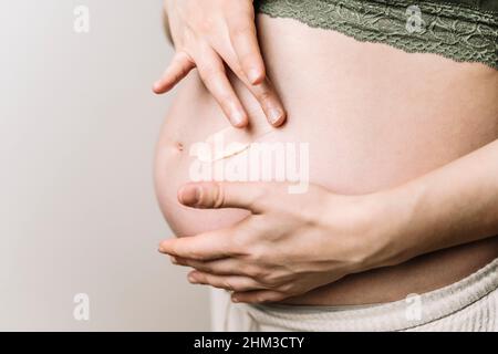 Une femme enceinte utilise une crème pour les marques d'étirement.Prévention des marques d'étirement sur l'abdomen et les jambes, soins de la peau pendant la grossesse.Photo de haute qualité Banque D'Images