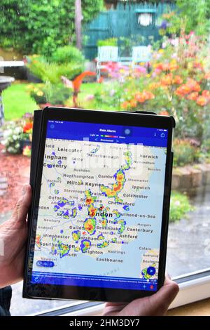 Les données de l'application de radar en couleur en temps réel pour ipad montrent les précipitations sur la carte locale, la femme attend que le temps humide s'efface sur la fenêtre de la maison revenir à jardinage Essex Royaume-Uni Banque D'Images