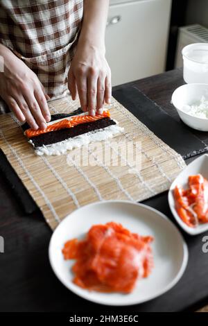 Une jeune femme enroule les ingrédients du rouleau de sushi sur un tapis de bambou Banque D'Images