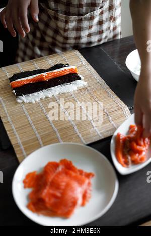 Une jeune femme enroule les ingrédients du rouleau de sushi sur un tapis de bambou Banque D'Images