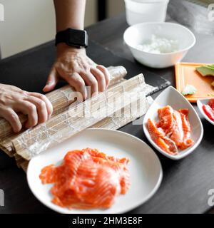 Une jeune femme enroule les ingrédients du rouleau de sushi sur un tapis de bambou Banque D'Images