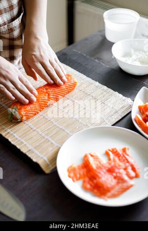 Une jeune femme enroule les ingrédients du rouleau de sushi sur un tapis de bambou. Banque D'Images