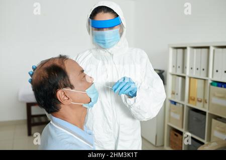 Infirmière médicale dans un équipement de protection à l'aide d'un écouvillon pour prélever un échantillon du virus coronavirus chez un patient potentiellement infecté Banque D'Images