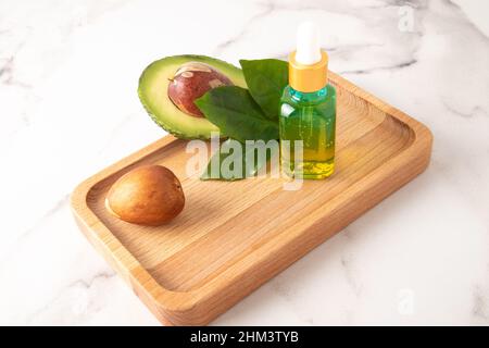 le concept d'huile d'avocat biologique naturelle pour le soin de la peau dans une bouteille de verre sur un plateau en bois avec des fruits d'avocat Banque D'Images