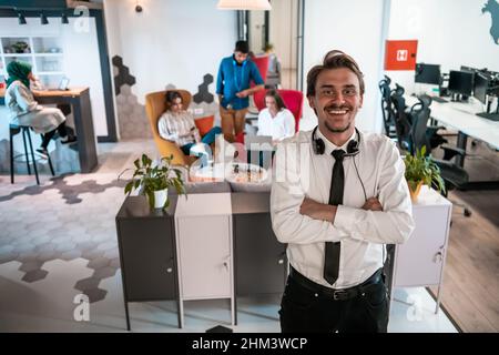 Portrait d'un homme d'affaires avec un casque autour de son cou et de ses collègues à l'arrière-plan au bureau de démarrage occupé Banque D'Images