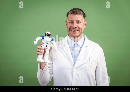 Un scientifique à la couche blanche tient un petit robot blanc en main et se tient devant un fond vert Banque D'Images