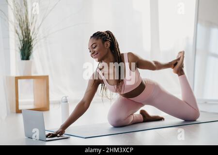 Jeune femme afro-américaine sportive qui s'étire près d'un ordinateur portable à la maison Banque D'Images