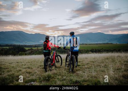 Vue arrière de deux cyclistes seniors marchant et poussant des vélos électroniques en plein air dans la forêt en automne. Banque D'Images