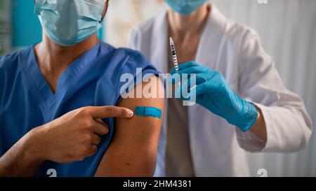 Gros plan d'un médecin méconnaissable montrant un bandage sur son bras après la vaccination. Banque D'Images