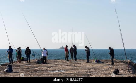 Cova Vapor, Portugal - 6 février 2022 : pêcheur sur la jetée avec Farol do Bugio dans le fond lointain Banque D'Images