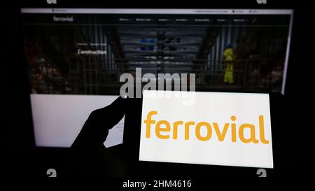 Personne tenant un téléphone portable avec le logo de la société espagnole de construction Ferrovial sa à l'écran en face de la page web d'affaires. Mise au point sur l'affichage du téléphone. Banque D'Images