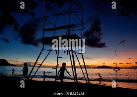 Enfants jouant à la plage de beau Vallon sous une tour de maître-nageur au coucher du soleil, île de Mahé, Seychelles. Banque D'Images