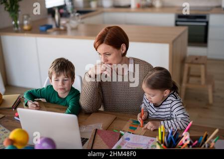 Mère de petits enfants les supervisant lorsqu'ils apprennent à distance et font leurs devoirs à la maison. Banque D'Images