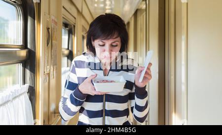 Une femme souriante marche le long du couloir le train avec un paquet de nouilles instantanées certifiées. Banque D'Images