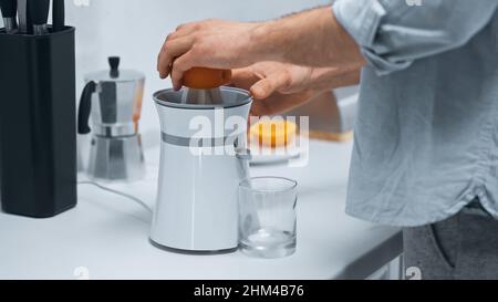 vue rognée d'un homme pressant de l'orange frais sur la centrifugeuse électrique près du verre Banque D'Images