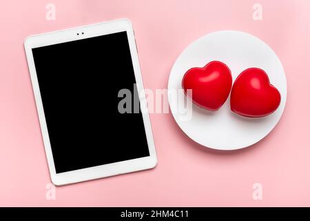 Tablette pour choisir des cadeaux, fait l'achat, deux coeurs rouges sur table rose vue du dessus plat Lay liste d'achats de vacances, bonne Saint-Valentin, fête, en ligne Banque D'Images