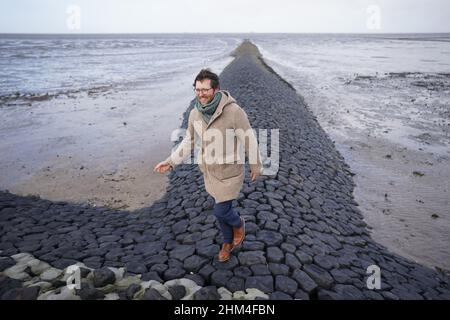 07 février 2022, Schleswig-Holstein, Nordstrand: Jan Philipp Albrecht (Bündnis 90/Die Grünen), Ministre de la transition énergétique, de l'agriculture, de l'environnement, de la nature et de la numérisation, traverse une groyne dans la mer des Wadden sur la côte de la mer du Nord après un événement médiatique sur la stratégie de protection côtière.Compte tenu de la hausse prévue du niveau de la mer et des ondes de tempête plus fortes, la poursuite du programme de renforcement des digues revêt une importance particulière pour l'État du Schleswig-Holstein.Selon le ministère, environ un quart de la superficie du Schleswig-Holstein est potentiellement en danger par la tempête sur Banque D'Images