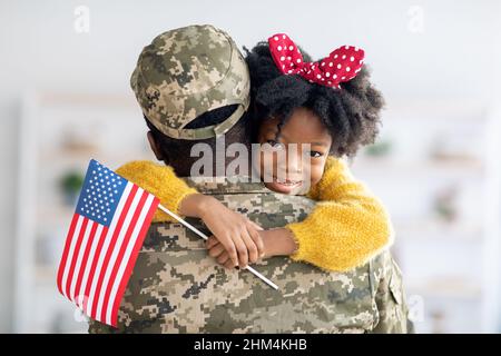 Adorable petite fille noire tenant un drapeau américain et embrassant le soldat papa Banque D'Images