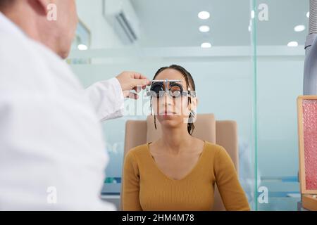 Médecin couvrant les yeux du patient portant des cadres d'essai et demandant à lire des lettres sur le dossier d'essai Banque D'Images