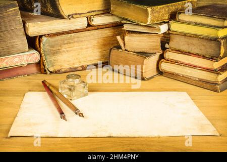 Image sépia de stylos plume vintage avec papier vierge devant de vieux livres sur une table Banque D'Images