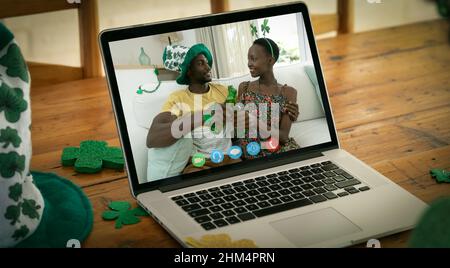 Webcam vue d'un couple afro-américain toaster des bières sur appel vidéo sur ordinateur portable sur table en bois Banque D'Images